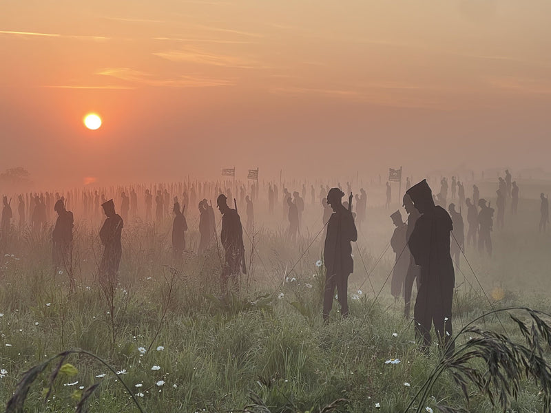 Silhouettes of people standing in a field at sunset with a hazy atmosphere. Photo credit Amanda Walden