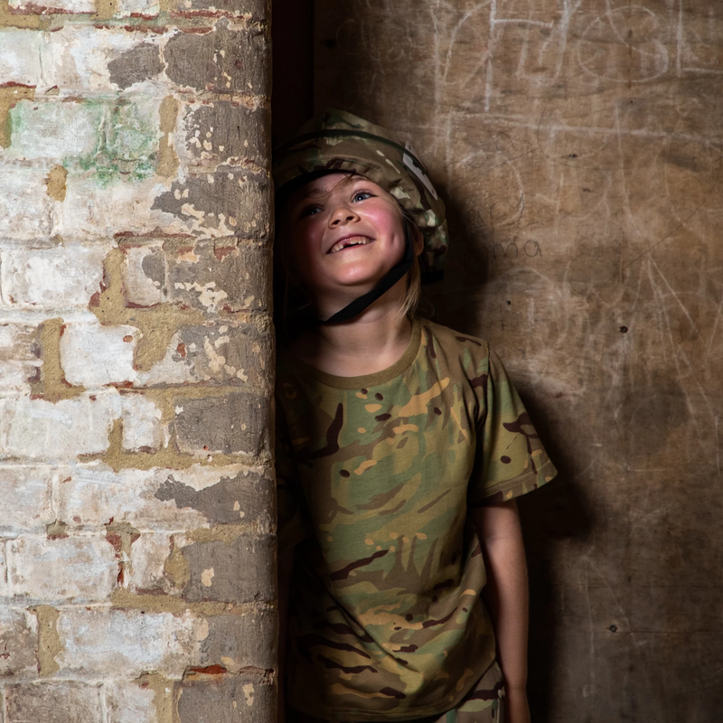 child hiding against wall wearing camo t shirt