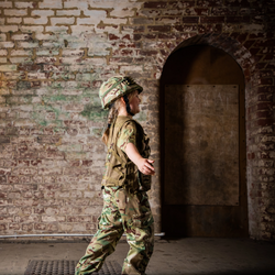 Child walking through abandoned looking building wearing camo trousers