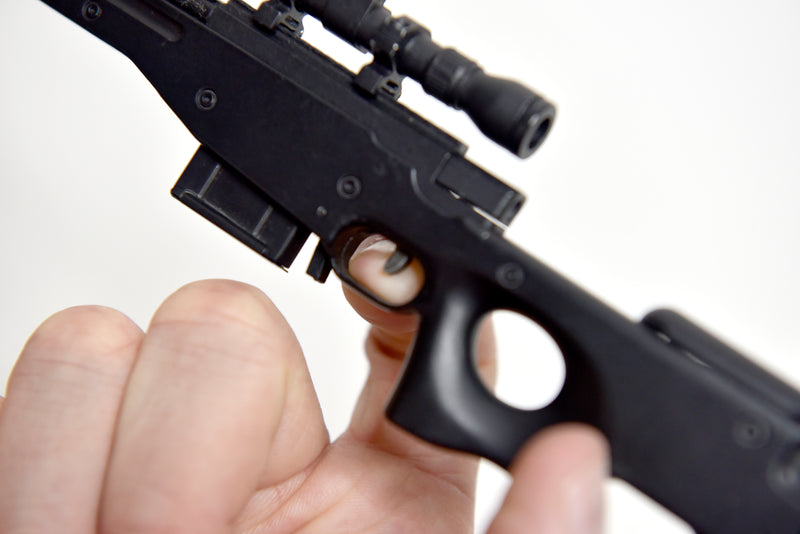 Closeup of the model L96A1. The model is being help up with a hand, and the trigger is being pulled by an index finger