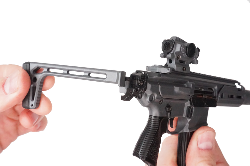 Stone grey SIG MCX model being held in two hands. The focus is on the stock which is being adjusted.