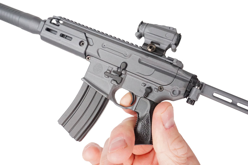 Stone grey SIG MCX model being held facing the left hand side. The model is being held in a right hand, the index finger on the trigger