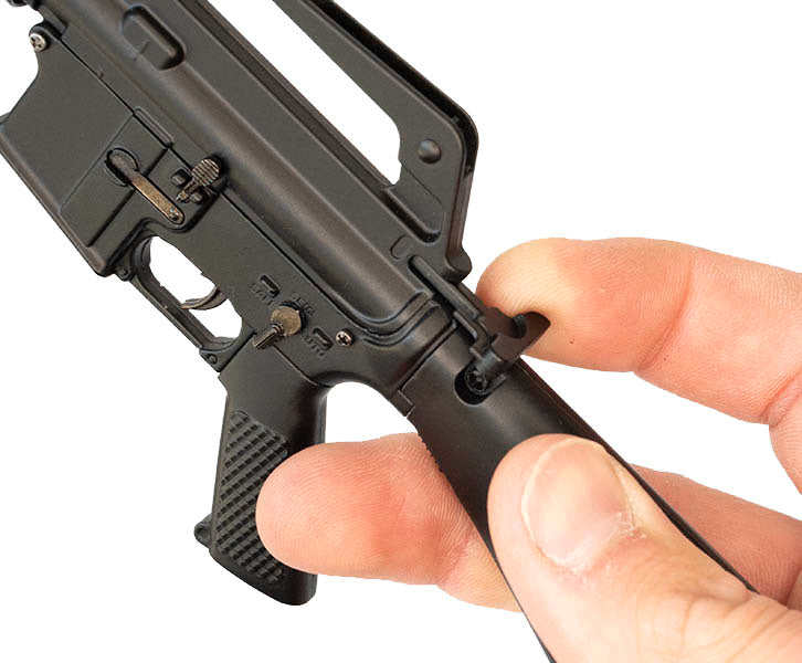 Close up of a hand holding the M16A1 model. The index finger is pulling back the hammer