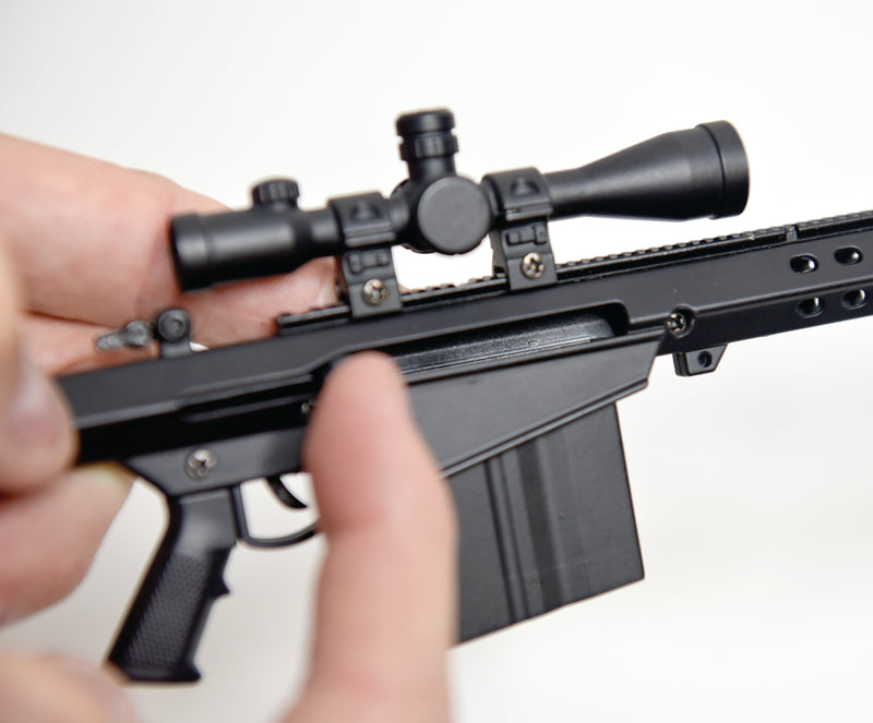 Closeup of the M82A1 model. The model is being held in two hands, demonstrating the small scale, and the right hand is pulling back the hammer.