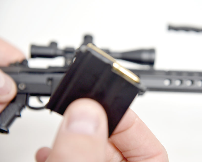Close up of a hand holding the model M82A1 magazine with ammo visible inside. The rest of the model is visible in the background.