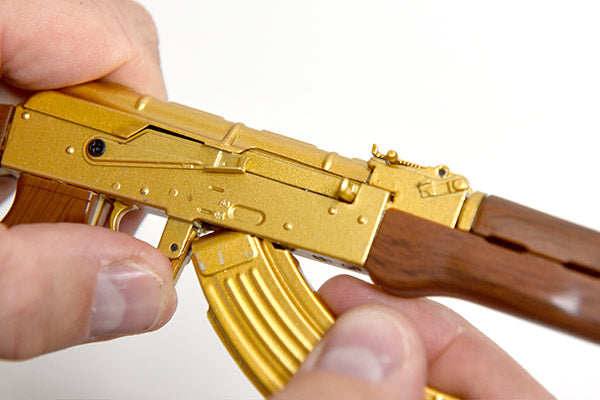 Close up of gold plated AK47 gun model, highlighting detail. Model is being held with two hands, demonstrating small scale