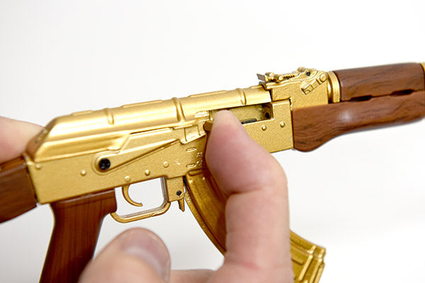 Close up of gold plated AK47 gun model. Model is being held with two hands which are working the actions