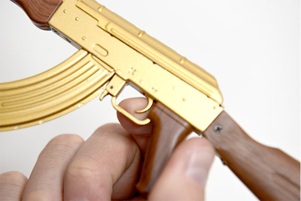 Close up of gold plated AK47 gun model. Model is being held and an index finger is pulling the trigger
