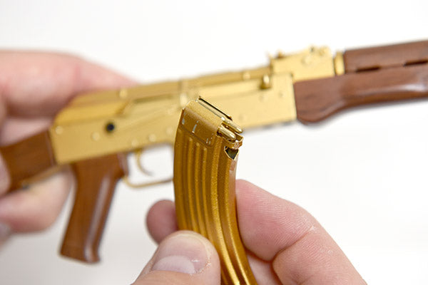Close up of gold plated AK47 gun model. The magazine is removed and the tiny rounds are visible inside it