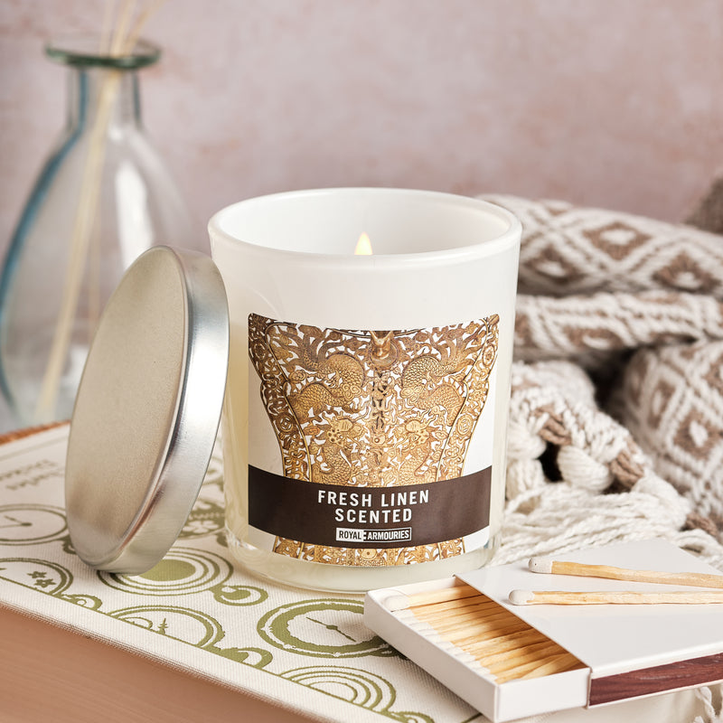 Fresh Linen Scented Candle - Processional Fan displayed with matches and a blanket with reed defuser in the background