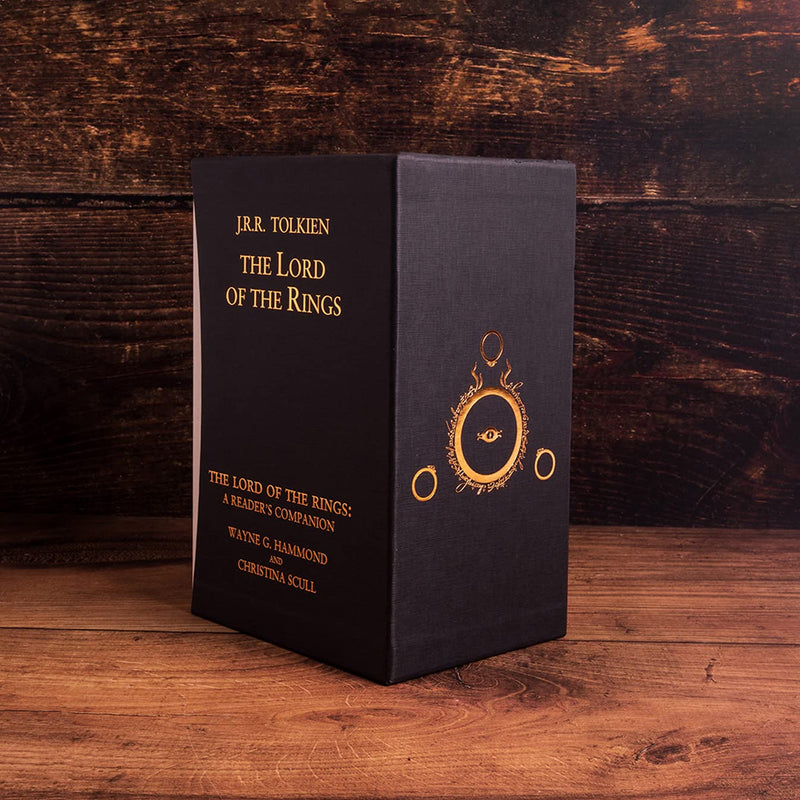back view of the special edition lord of the rings boxed set. the set is black with gold writing. There is a gold emblem design on the very back pane. It is displayed on a rustic wooden bench.