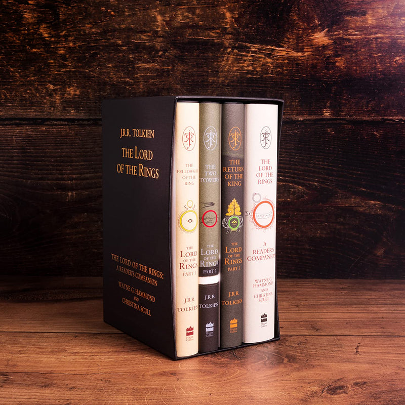 Four book boxed set of the Lord of the rings trilogy in a black box with gold writing. The books are in neutral tones with vintage style designs on them. It is displayed on a rustic wooden bench