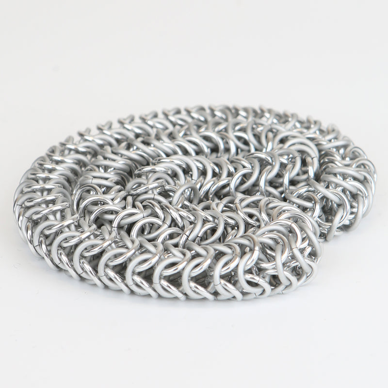 Intricately linked chunky silver chainmail necklace displayed in neatly coiled pile