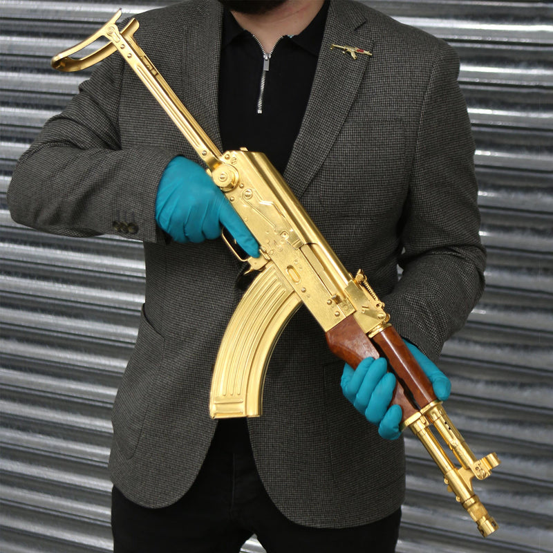 Golden Kalashnikov AK-47 Pin Badge on jacket lapel of person holding the original from the Royal Armouries Collection