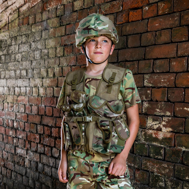 child dressed in camo mtp t-shirt, vest, trousers and helmet against brick wall