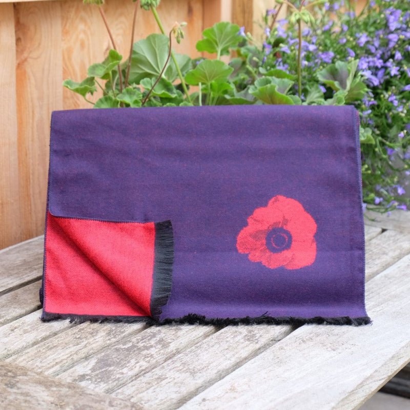 Navy blue scarf with a red poppy design on a wooden surface with plants in the background