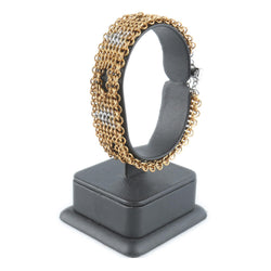 Gold chainmaille bracelet on a black stand against a white background