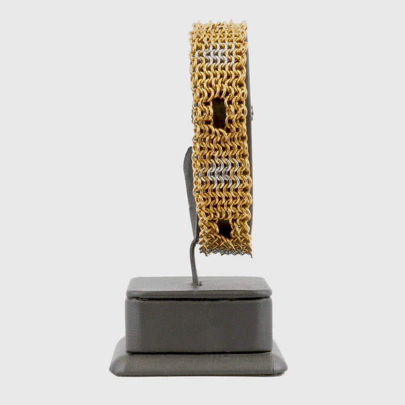 Gold and silver chainmaille bracelet on a black stand against a white background