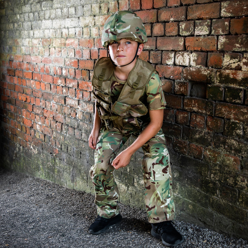 child crouched by exposed brick wall wearing camo trousers